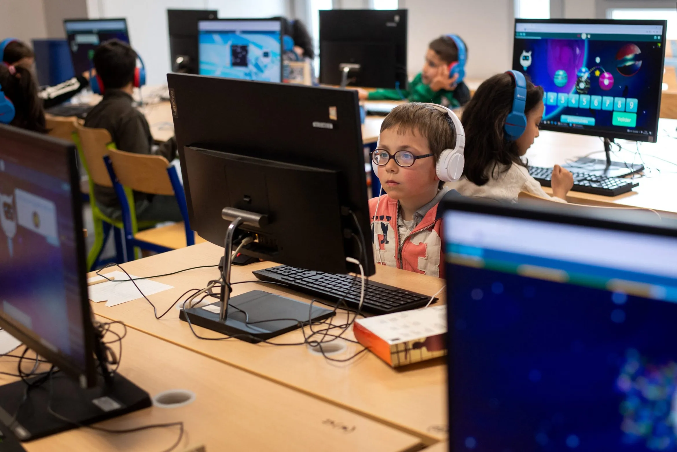 children in a computer lab wearing headphones and working on computers